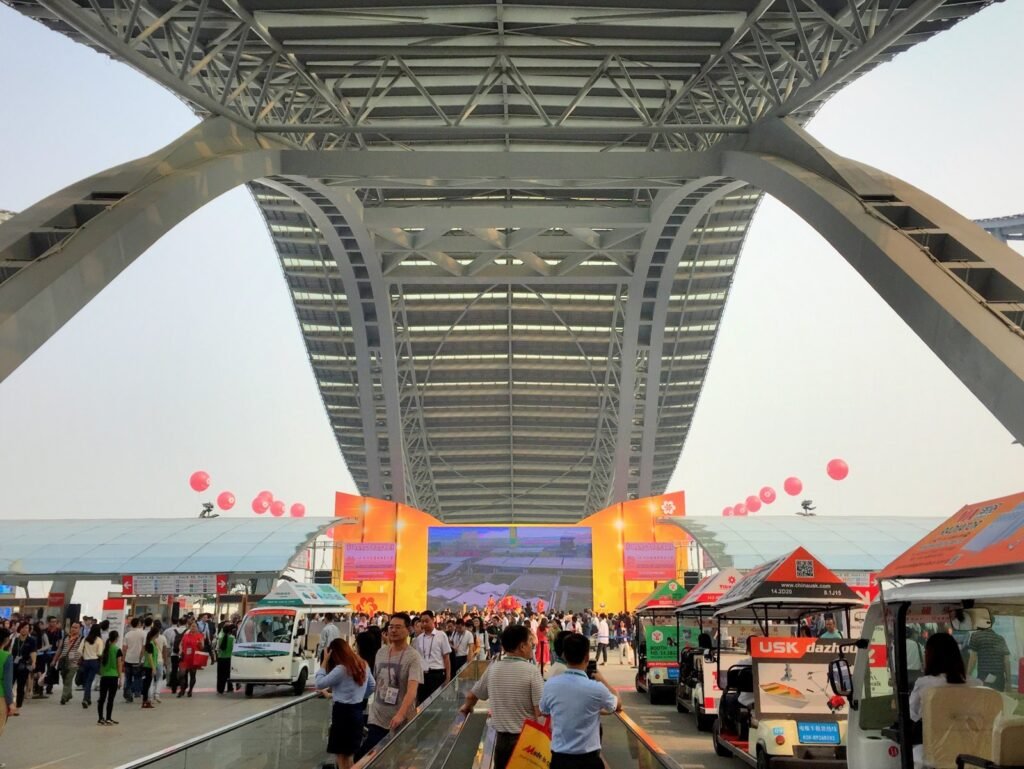 Buyers arriving under the steel arches at the Canton Fair Complex entrance in Pazhou, Guangzhou, with moving walkways and electric shuttle carts