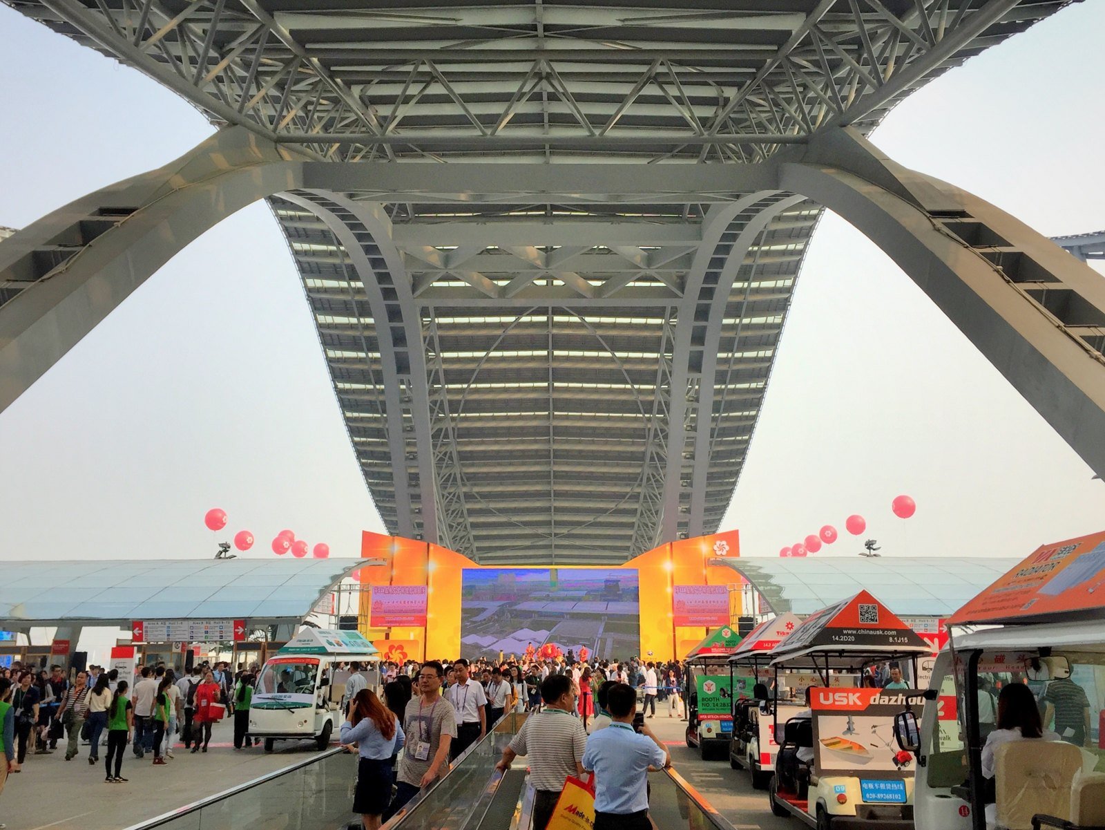 Buyers arriving under the steel arches at the Canton Fair Complex entrance in Pazhou, Guangzhou, with moving walkways and electric shuttle carts